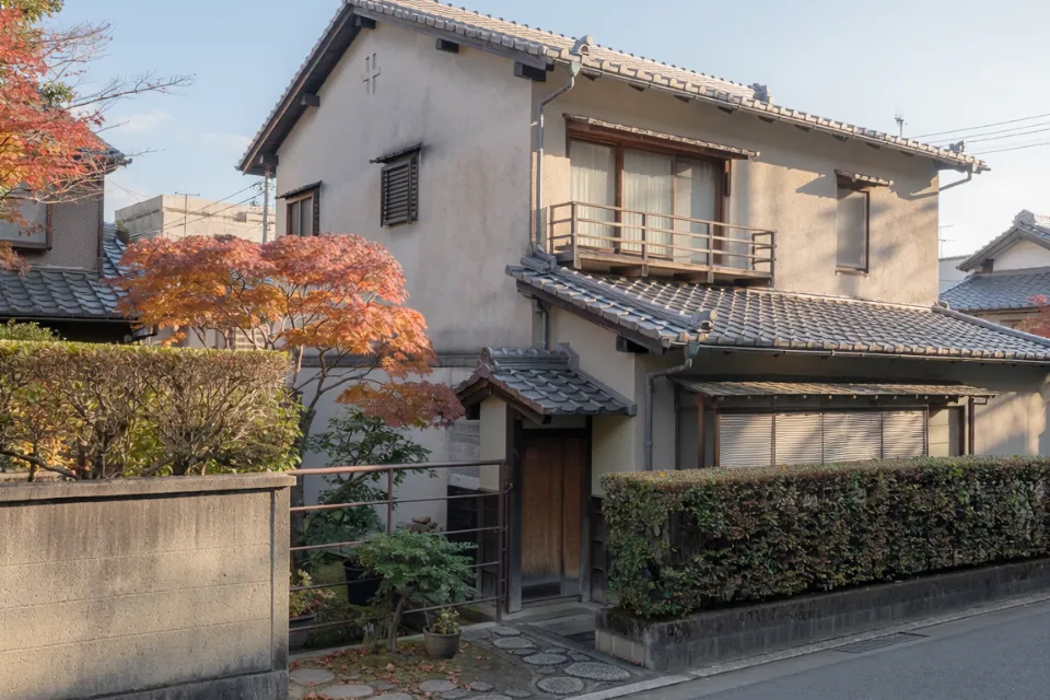 紅葉した木のある、瓦屋根の2階建ての一軒家